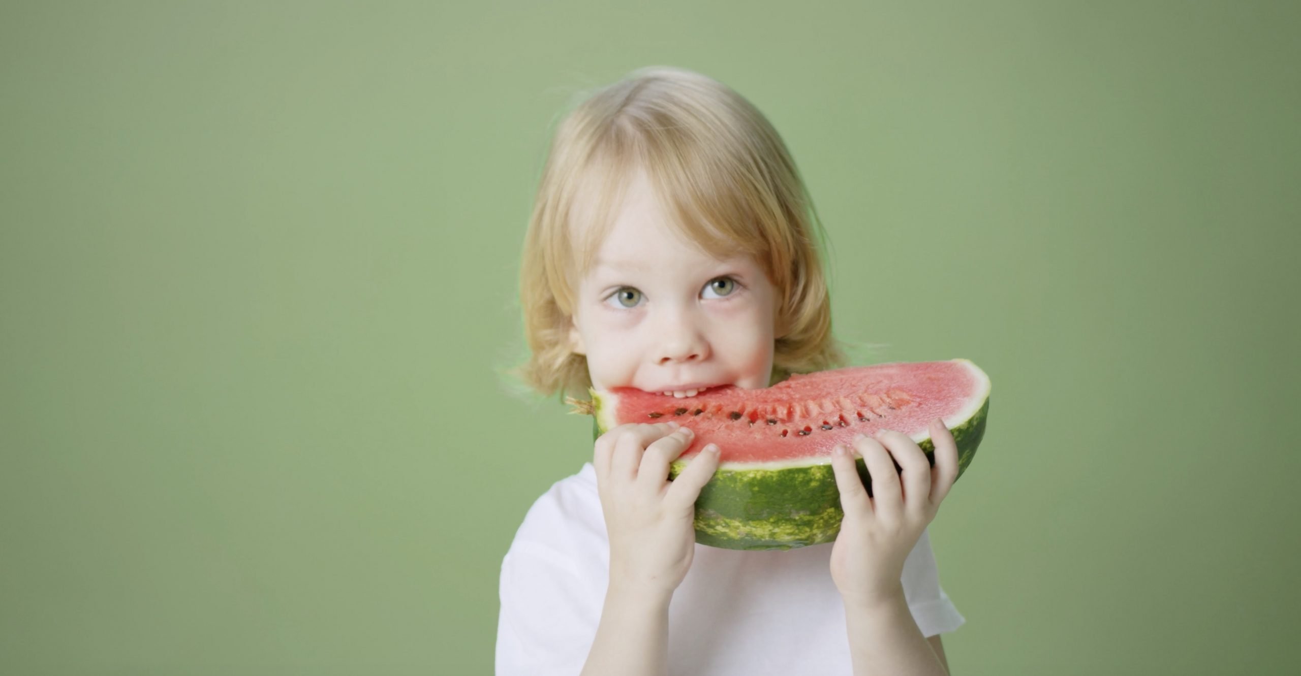 A young boy joyfully holds a slice of watermelon, savoring its refreshing taste on a sunny day.