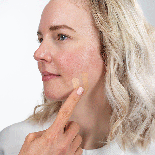 A model tests out shades on their jaw bone, a lighter shade is right for their skin tone.