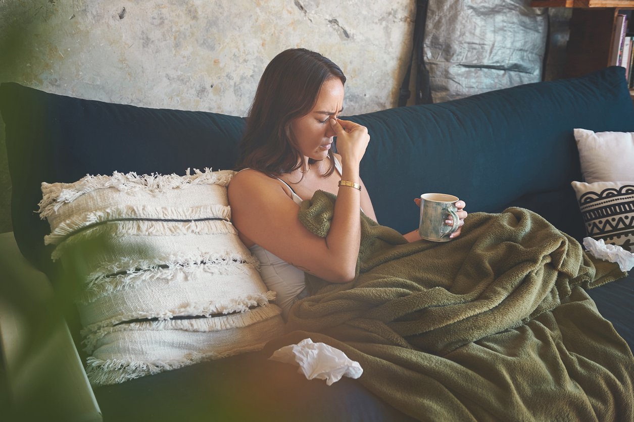 Woman sat on sofa feeling unwell which may be due to a weak immune system