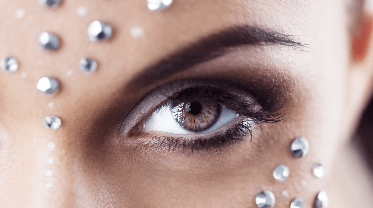 A close up of a woman's eye makeup, featuring face gems