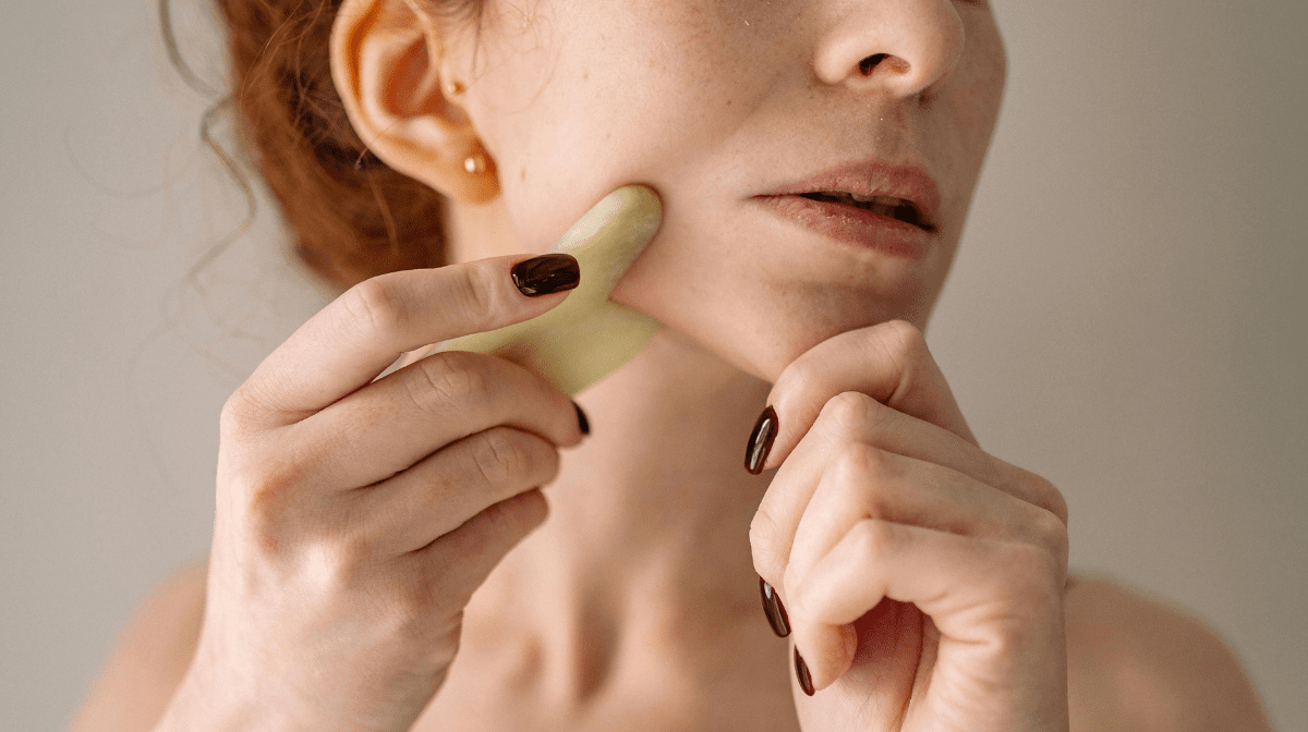 Woman gently scraping her gua sha tool against her jawline.