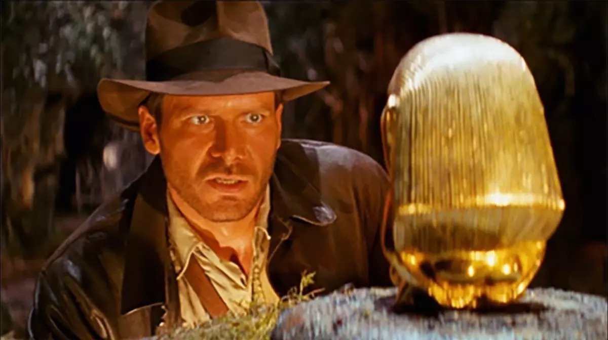 Indiana Jones wearing his iconic brown fedora hat in the Raiders of the Lost Ark, laying his eyes on the Chachapoyan golden fertility idol of Pachamama