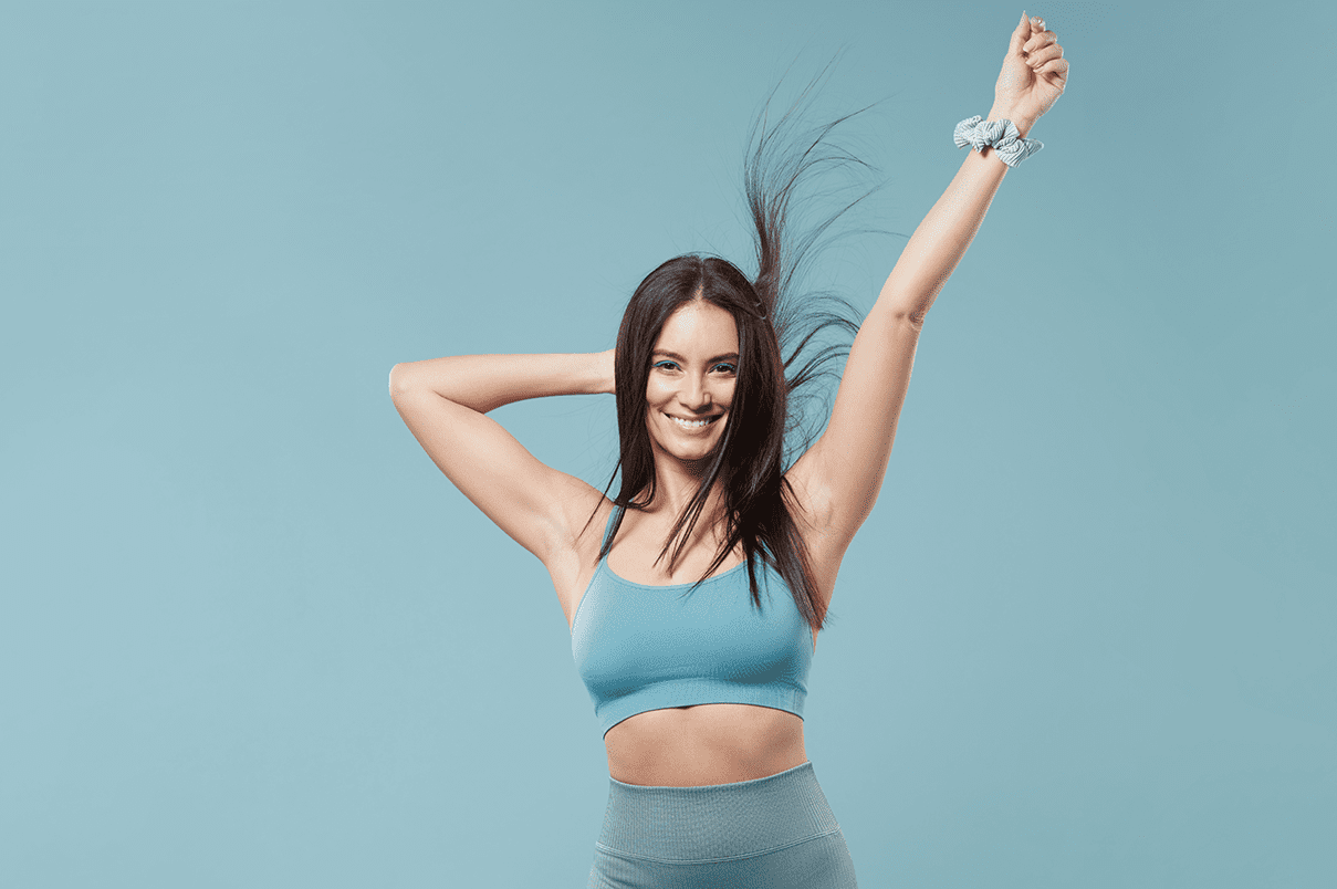 Woman smiling flicking sleek hair, blue background, showing confidence with a hand in the air.