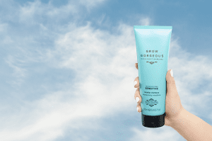 A hand holding up in the clouds the Grow Gorgeous dandruff fragrance-free and dermatologically tested sensitive replenishing conditioner.
