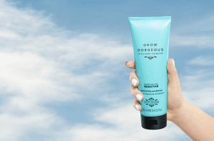 A hand holding up in the clouds the Grow Gorgeous dandruff fragrance-free and dermatologically tested sensitive micellar shampoo.