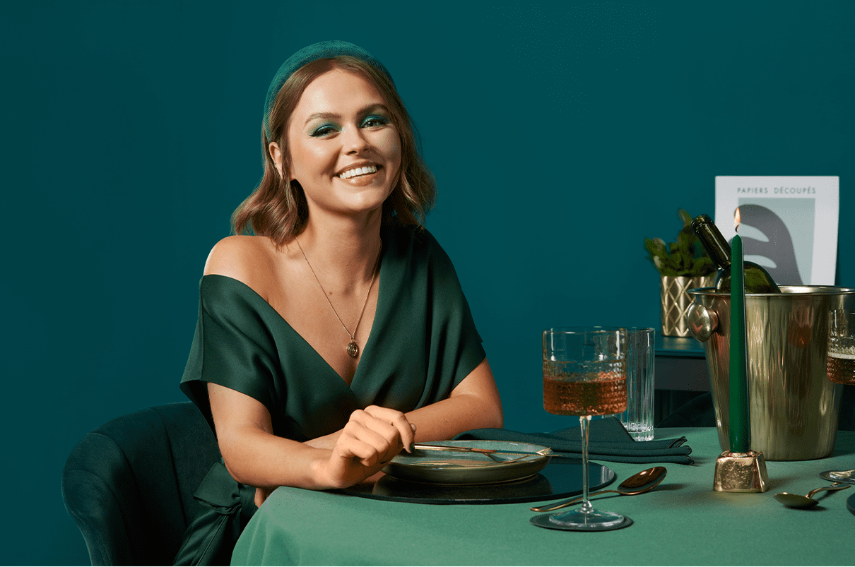 A woman with short straight hair sitting at a table for dinner with a glass of wine smiling