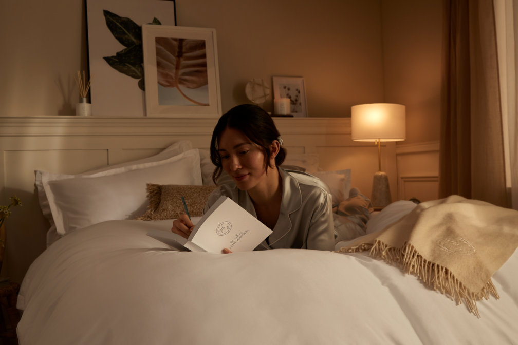 Woman in bed writing wellness new years resolutions in her diary.