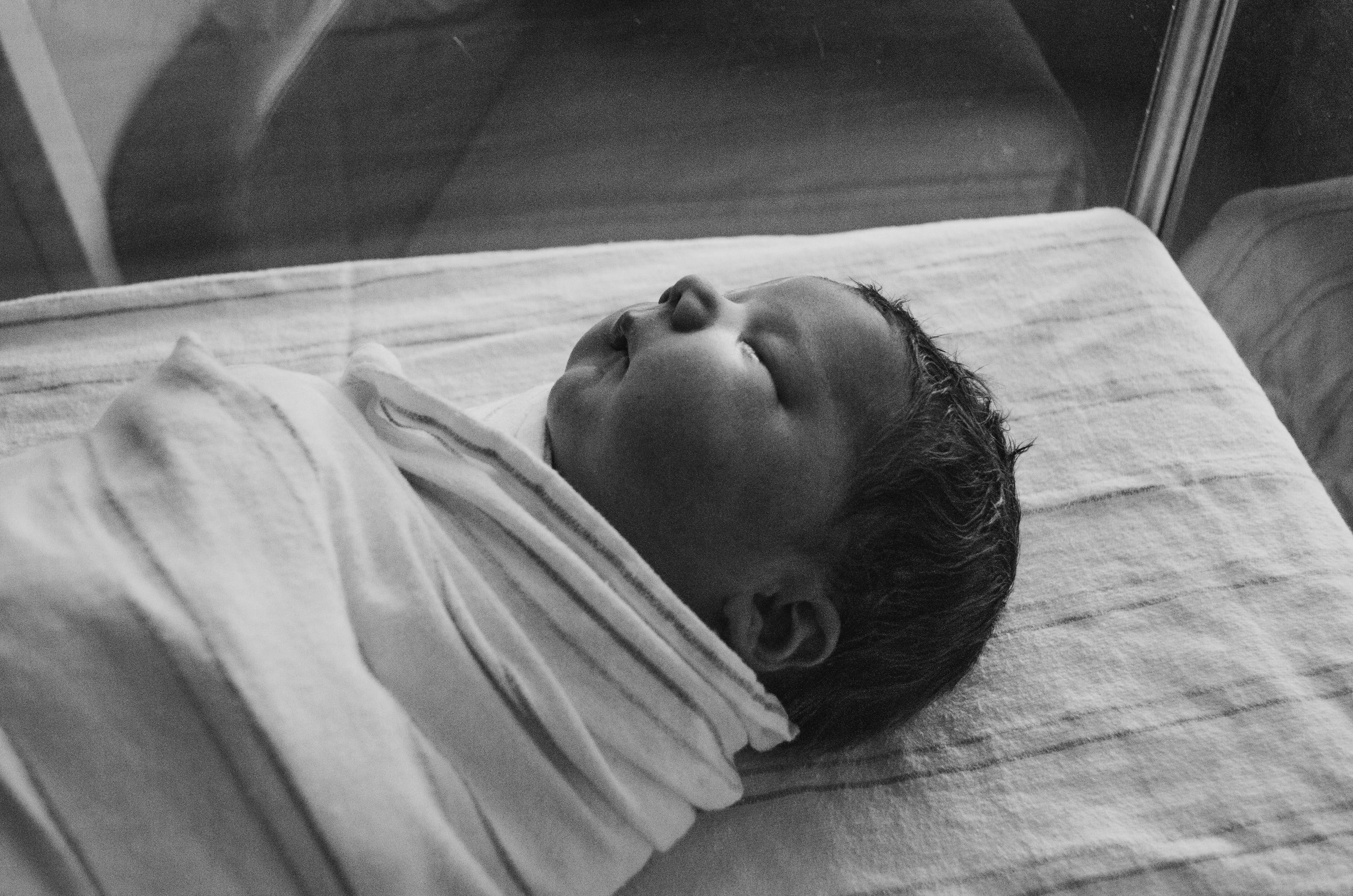 Baby asleep in plain crib wrapped in a white sheet