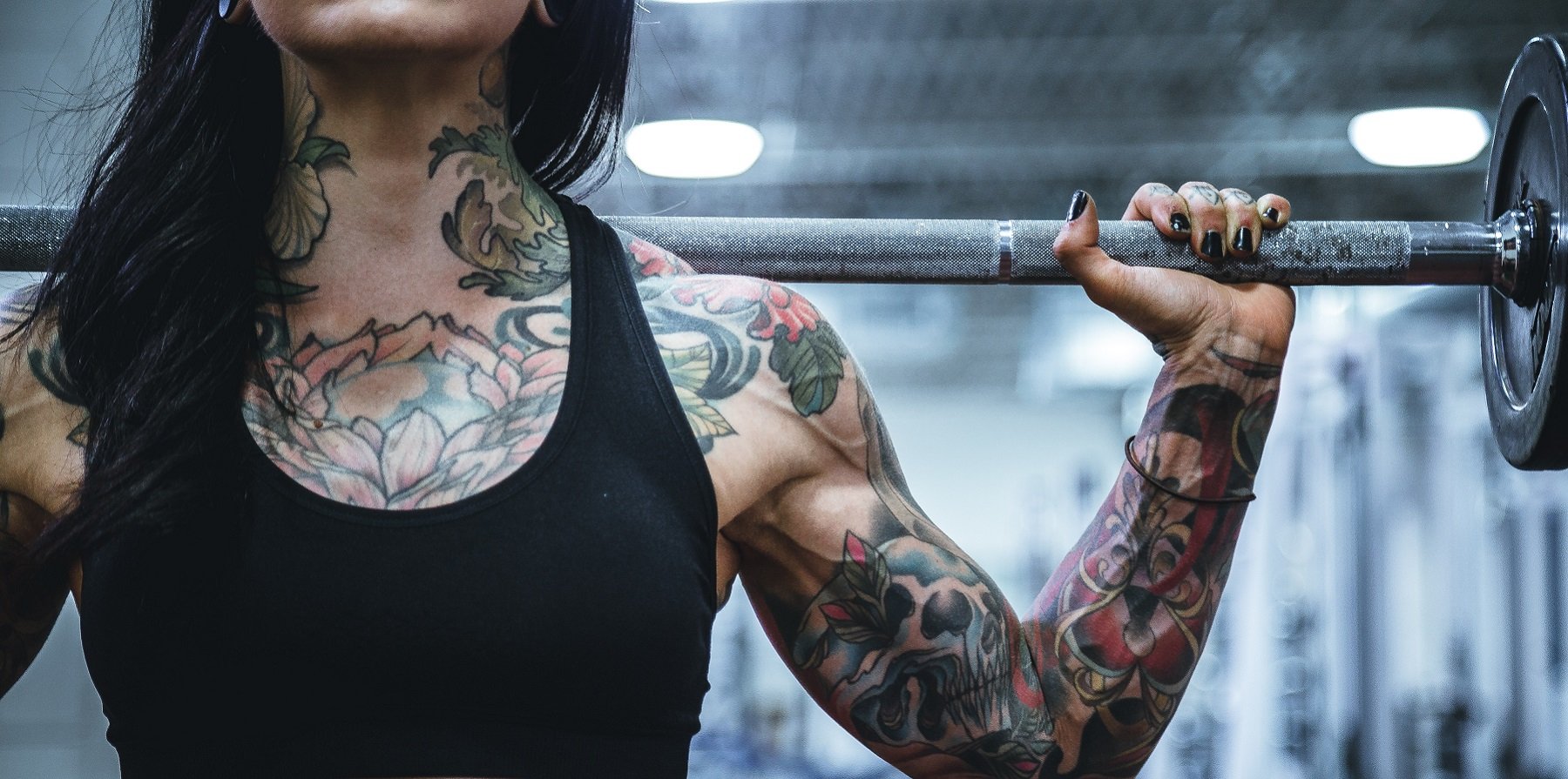 Torso of woman with tattoos holding barbell on shoulders