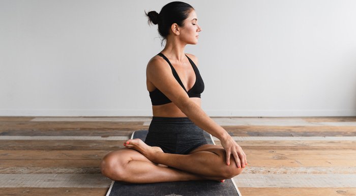 A woman sat on a mat on a wooden floor stretching and doing pilates.