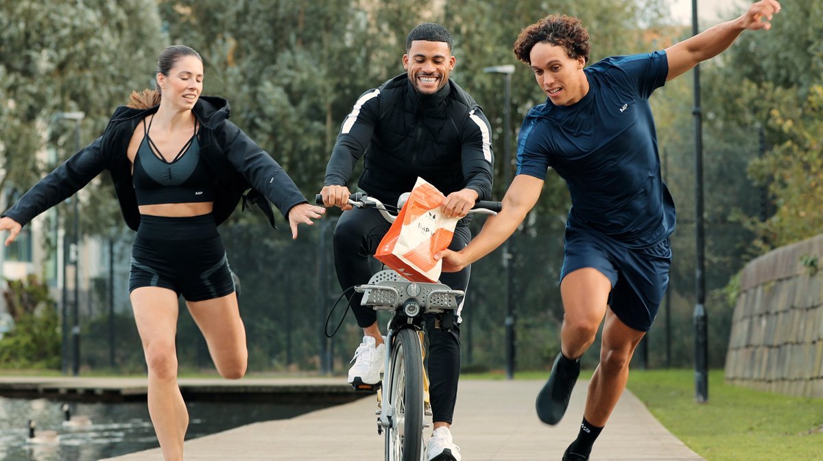 Runners wearing MP clothing running alongside a bicycle chasing for Impact Whey Protein from Myprotein.