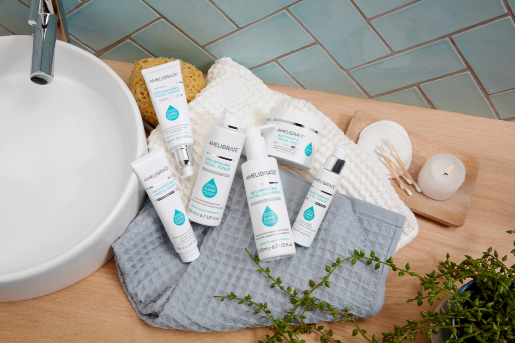 AMELIORATE skincare products displayed on towels beside a sink with candle and greenery.