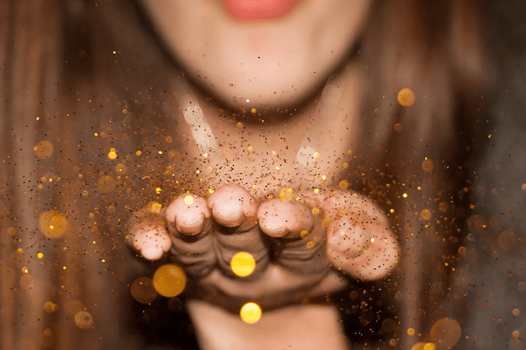 woman blowing gold glitter off hand