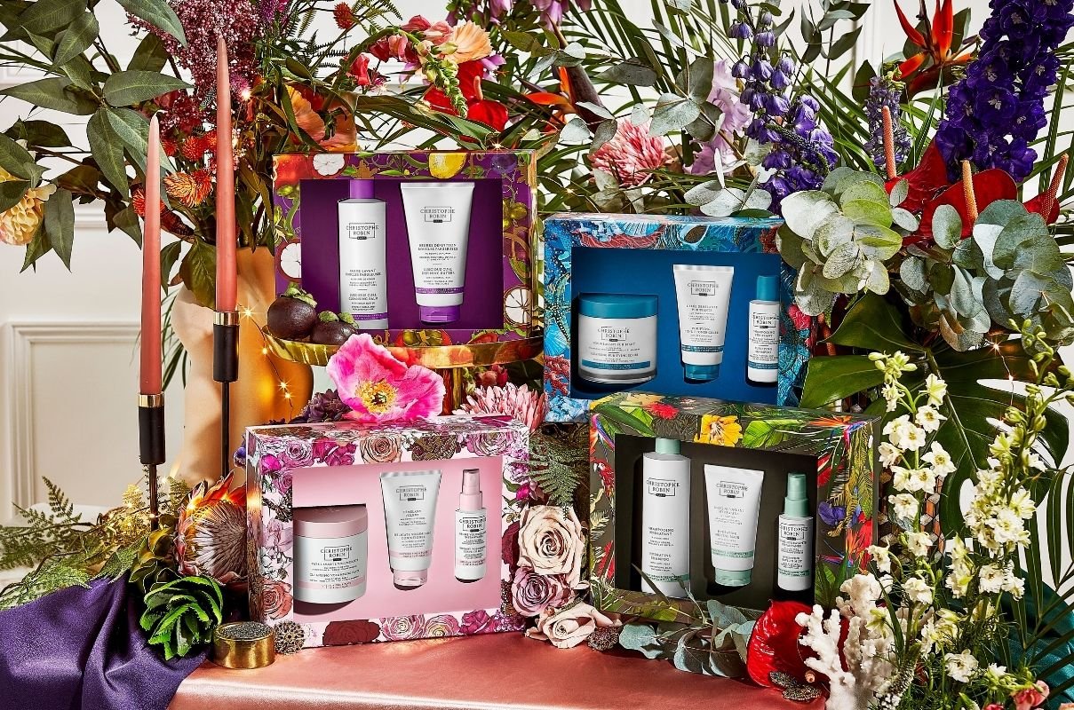Four different Christophe Robin hair product Christmas gifts in front of a huge colour display of flowers