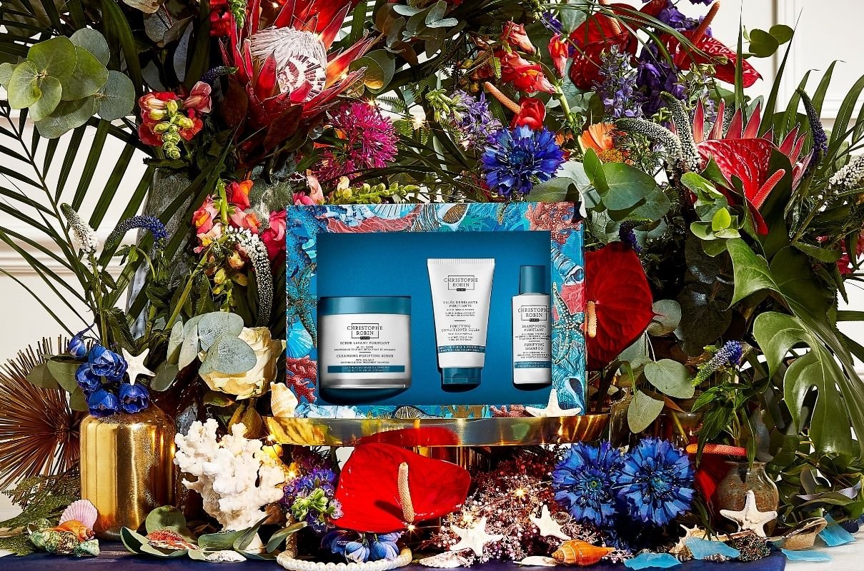 Hair Detox Ritual Christmas gift set in a square blue floral packaging in front of a huge display of colour flowers
