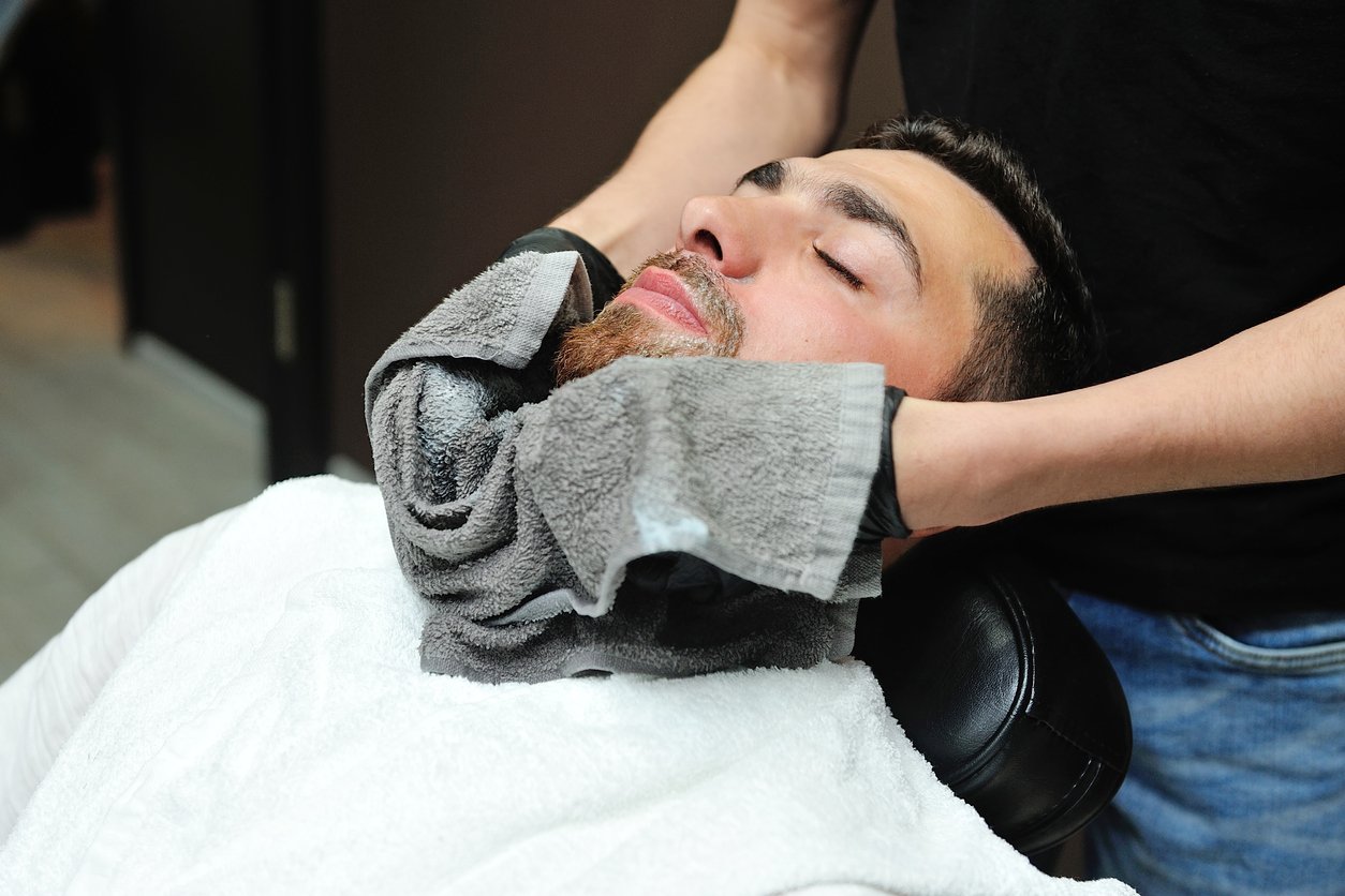 Man getting hot towel treatment to prep for against the grain shaving