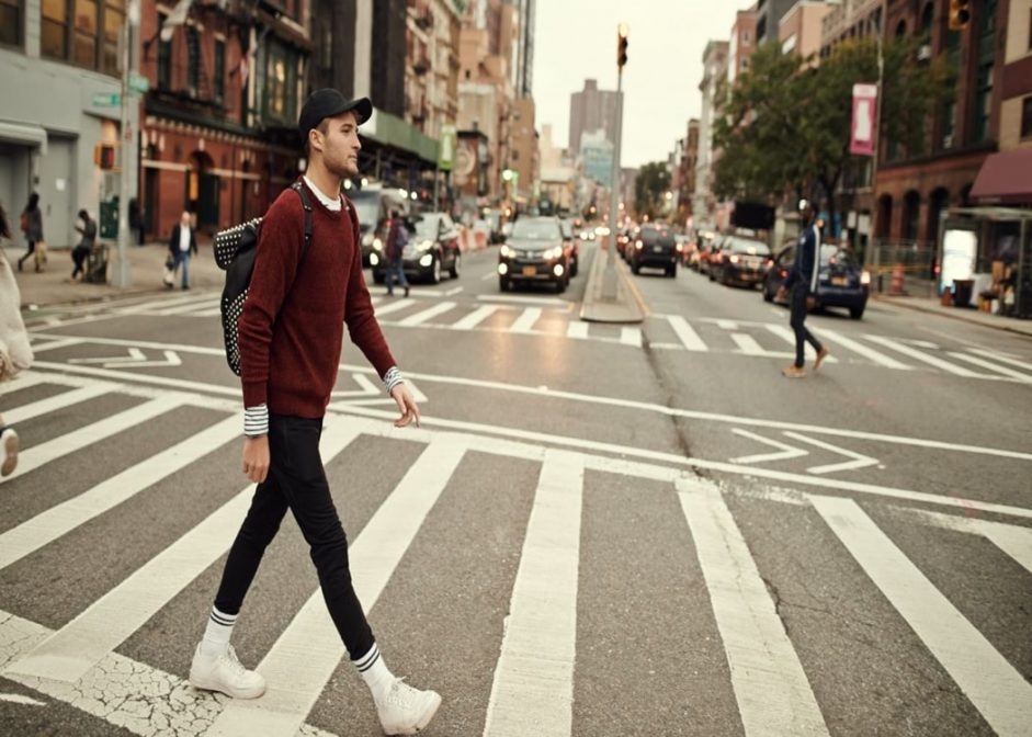 man crossing the road wearing a jumper over a t-shirt