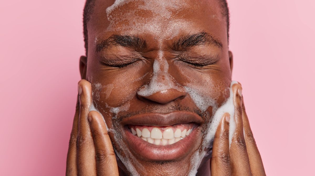 A man gently cleanses his skin with face wash against a pink background | Gillette UK