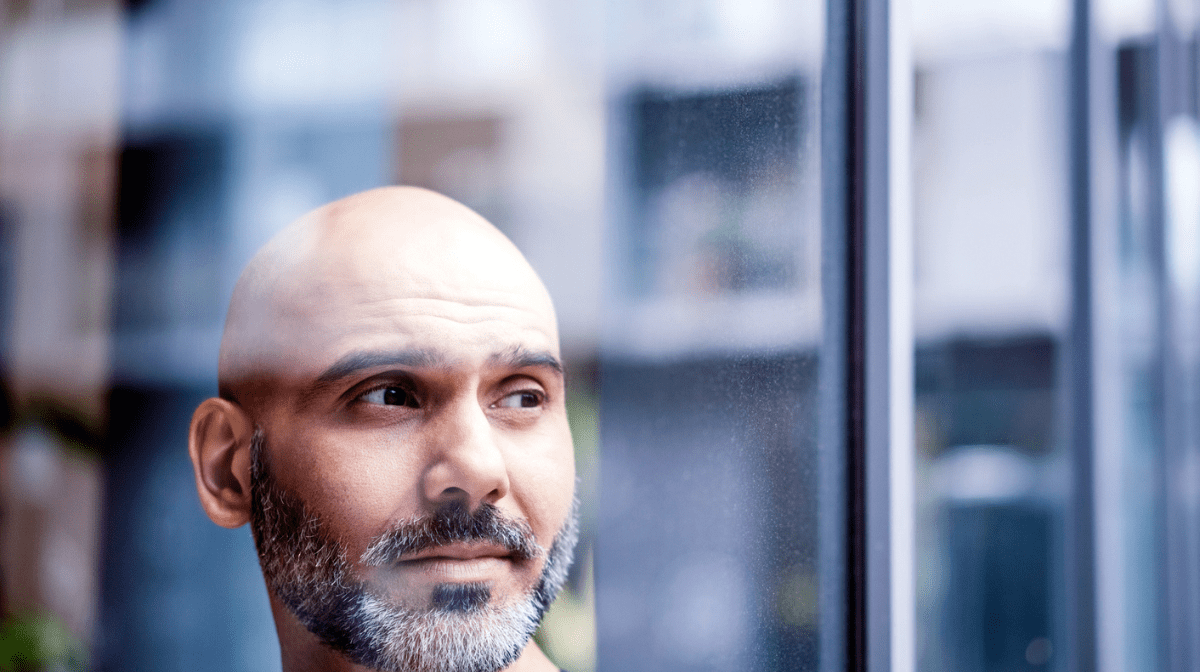 Man with bald head and beard looking through window 