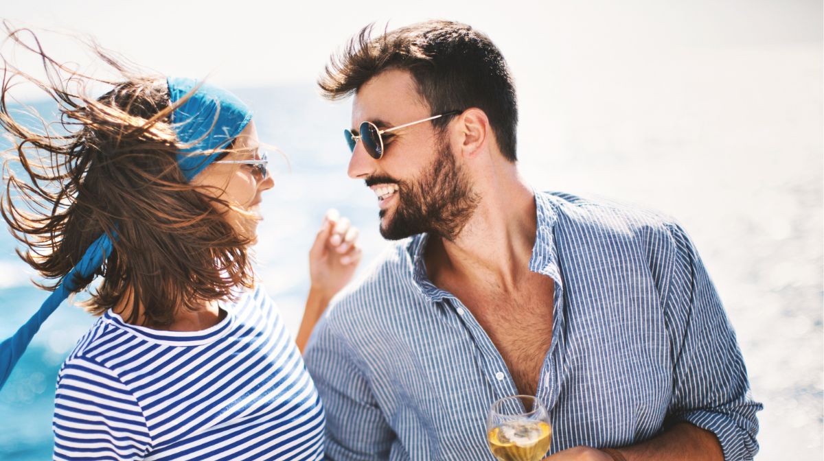 A young man with a beard laughs with his partner on the beach