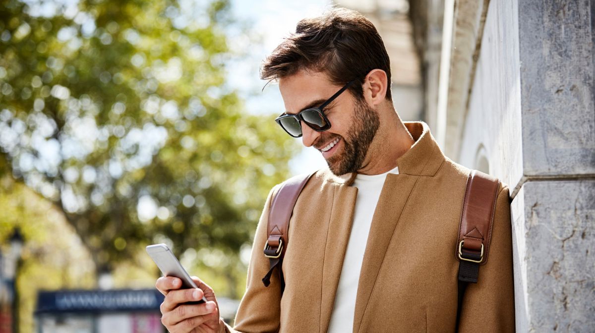A handsome, well-groomed man looks at his phone whilst wearing minimalist fashion basics.