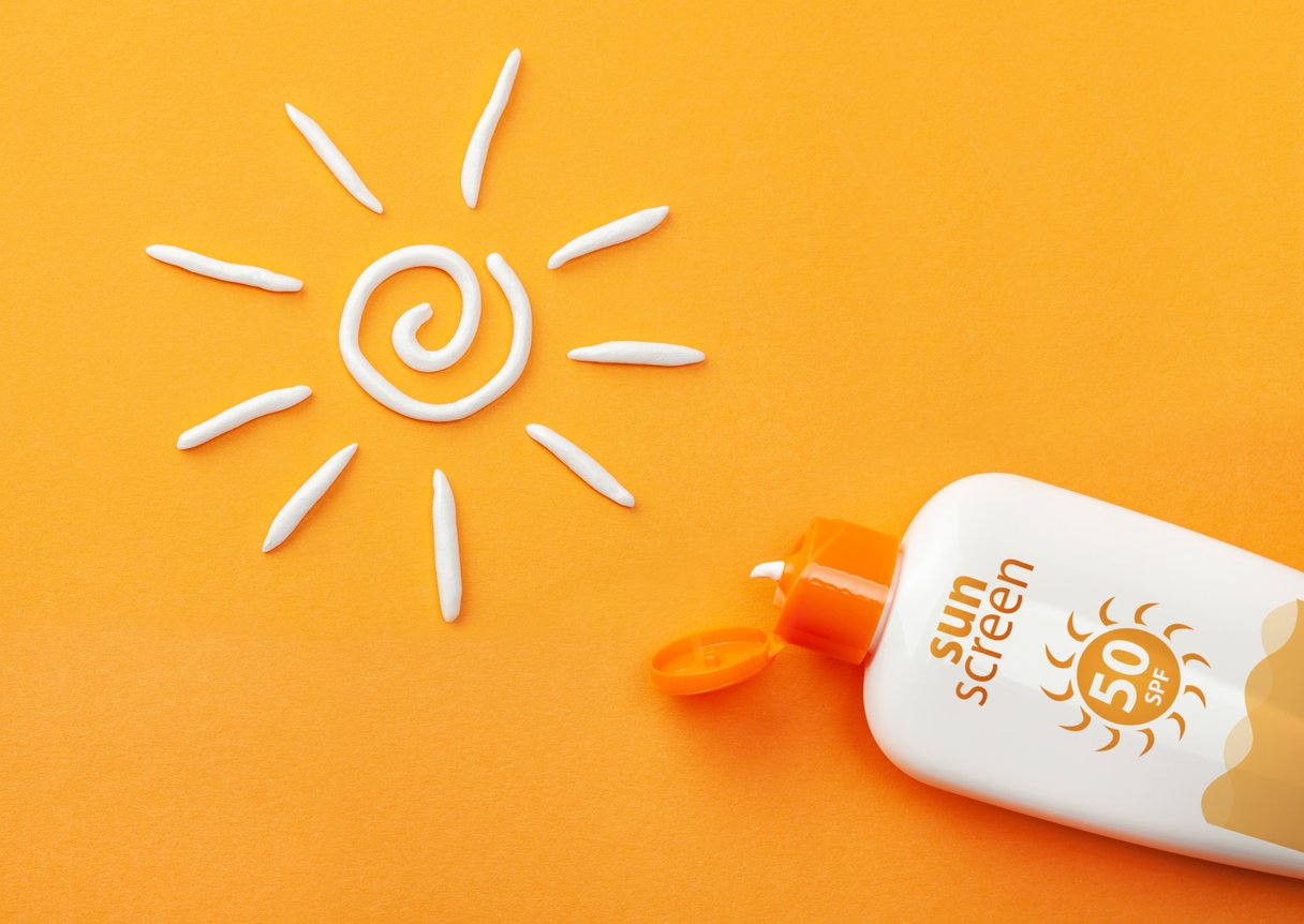 Sunscreen on orange background. Plastic bottle of sun protection and white sun-shaped cream.