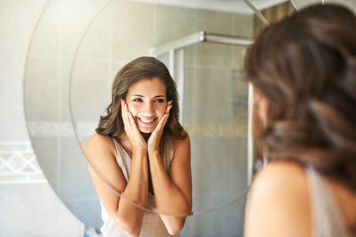 Woman smiling while looking into a mirror after dermaplaning | Venus UK