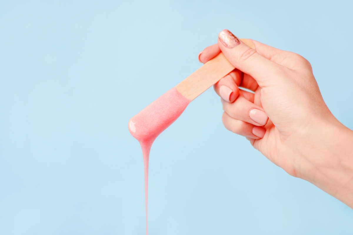 A hand holds a stick with hot wax dripping from it against a pale blue background | Venus UK