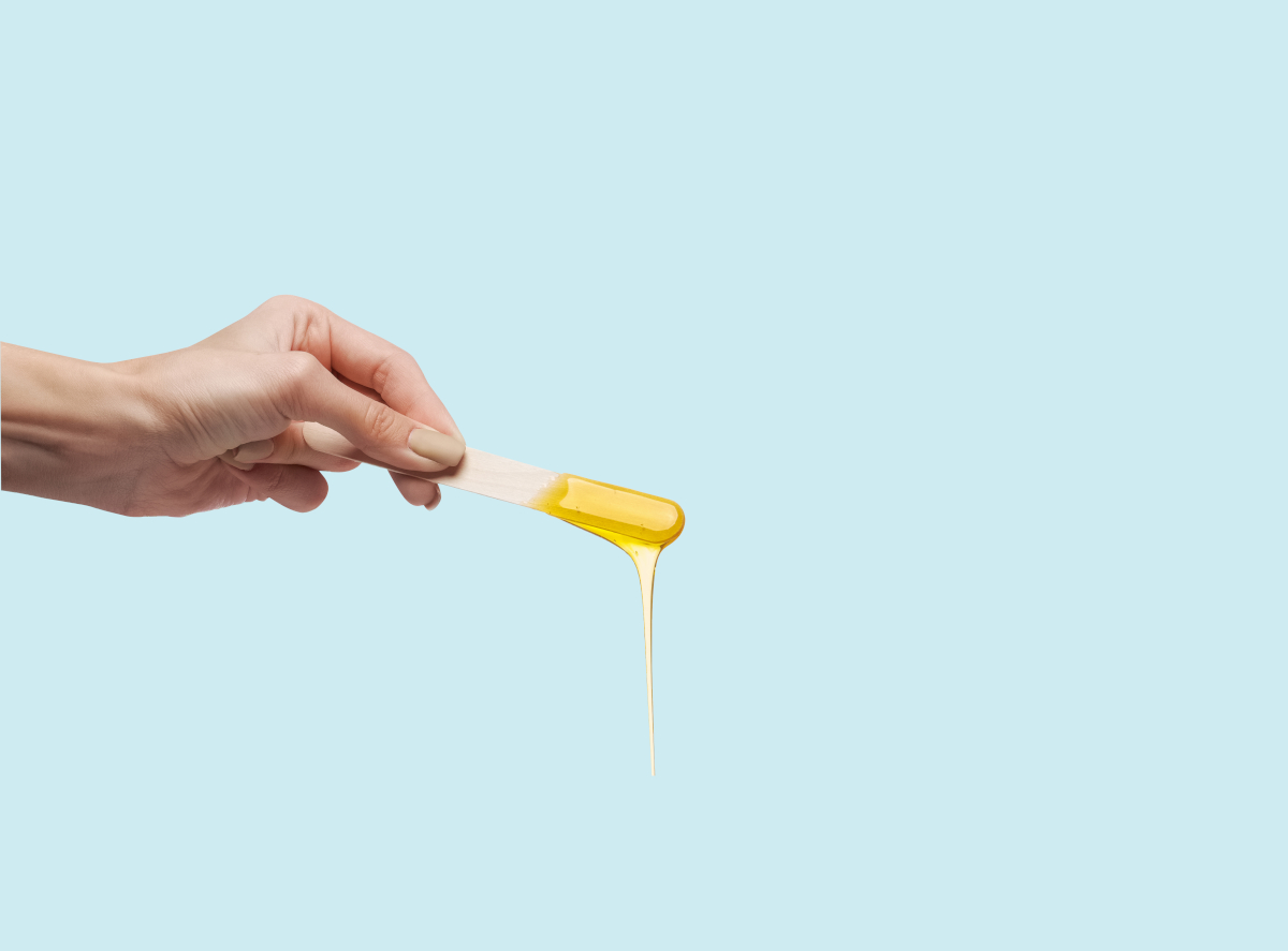 A hand holds a stick with hot wax dripping from it against a pale blue background | Venus UK