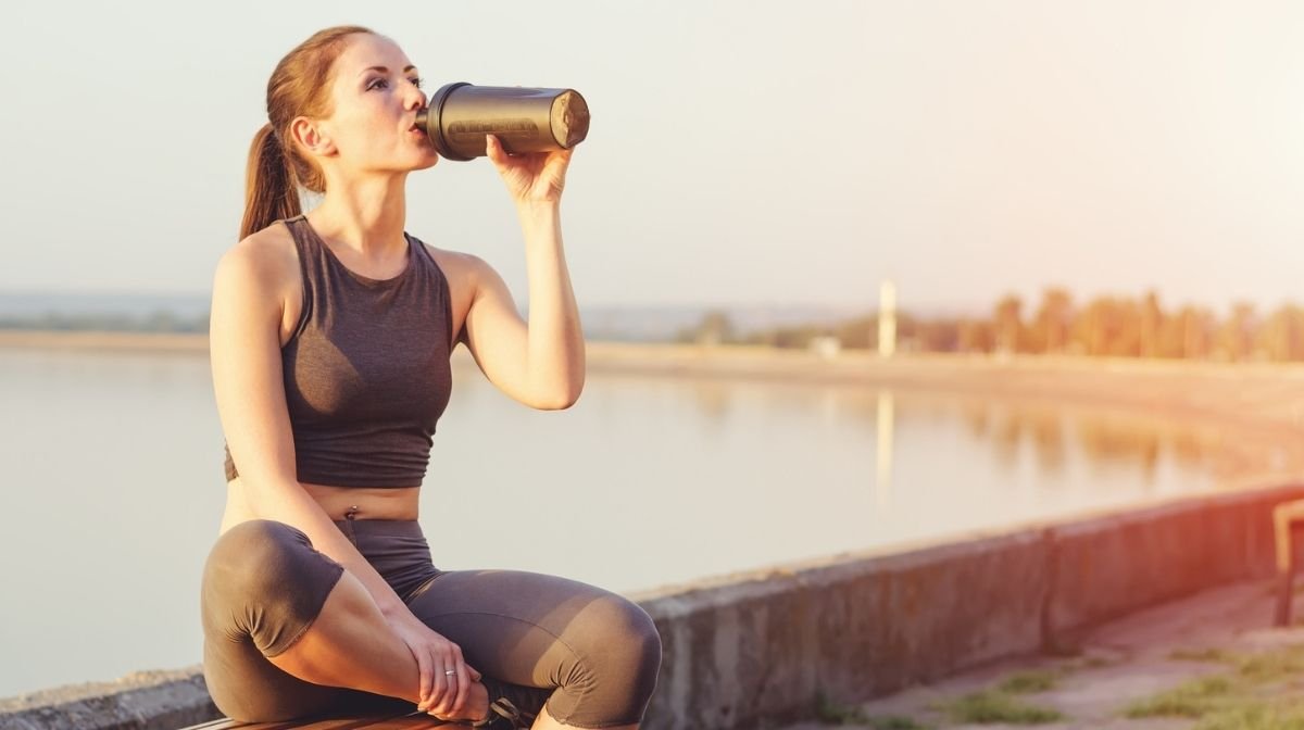 woman drinking protein drink while exercising outdoors