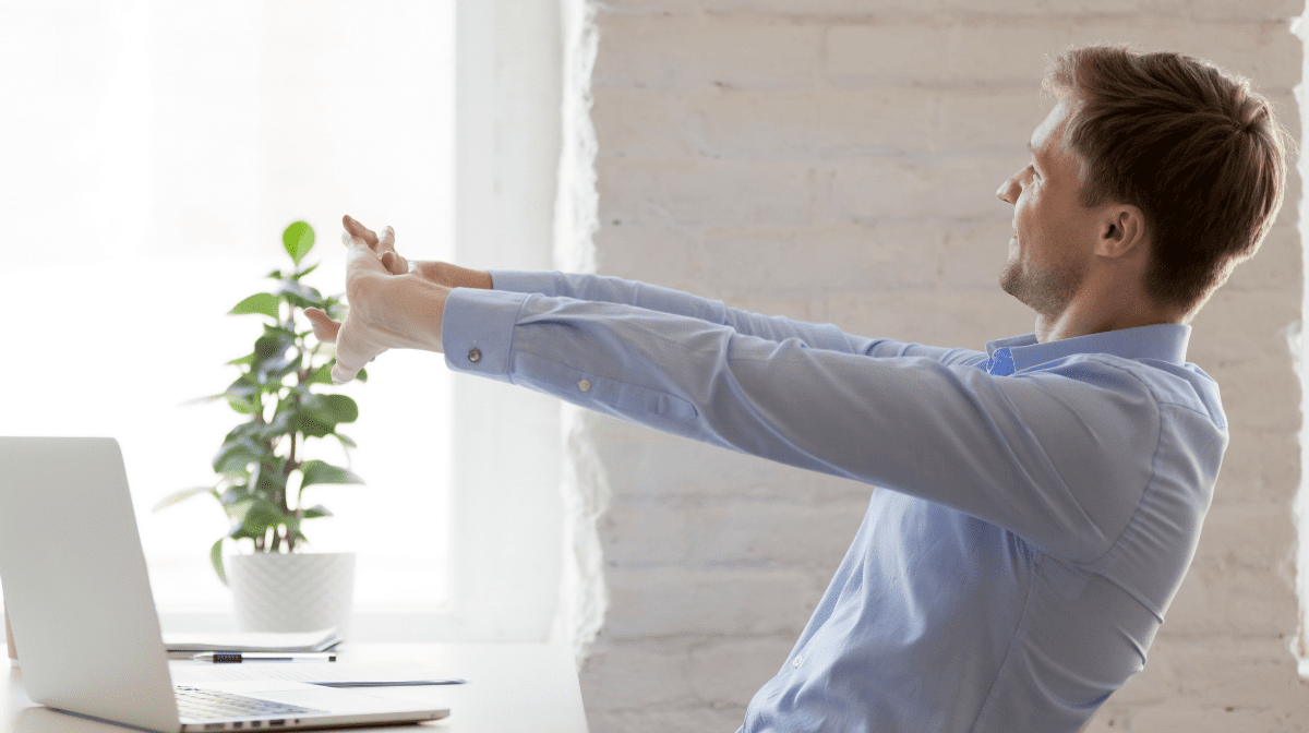 man stretching arms out at desk