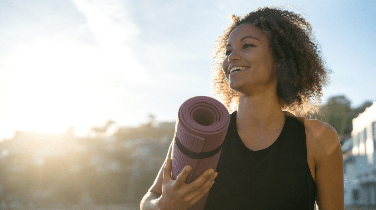 woman outdoors with yoga mat smiling