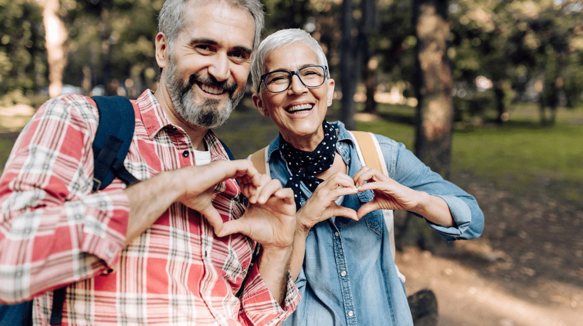 Mature couple in a park showing hearts