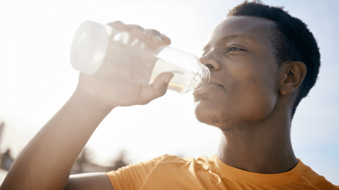 An active, African American man, drinking a bottle of water in the sun
