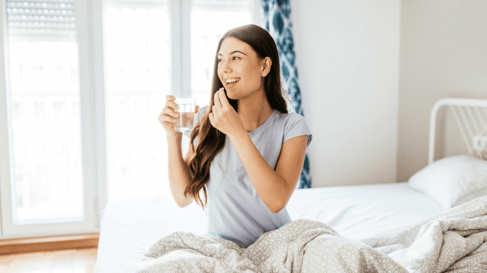 Women sat up in bed with a glass of water taking period supplements