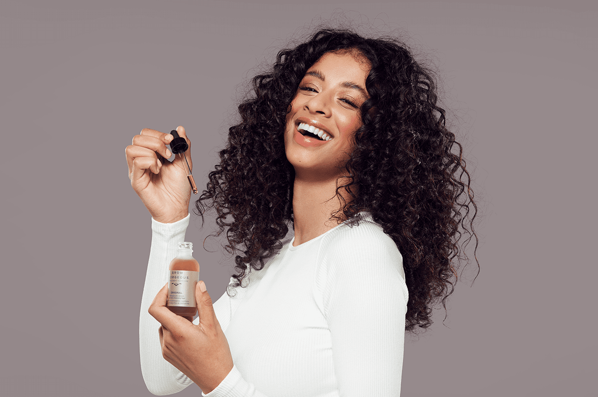Woman with thick curly hair holding up Grow Gorgeous density serum original bottle