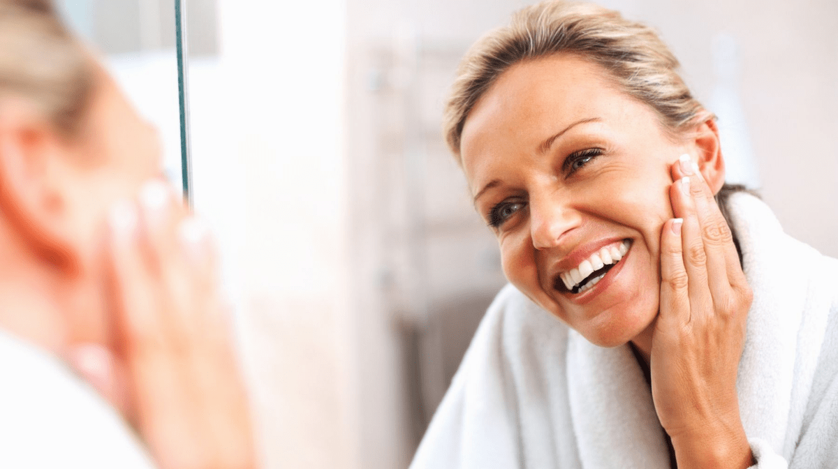 Woman happily admiring her skin in the mirror, pleased with the results she's seen from knowing how to properly treat and care for combination skin.