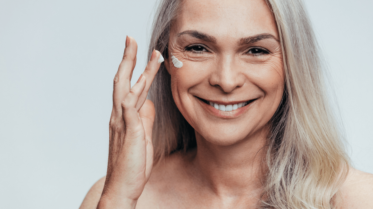 A woman applying sunscreen to her face. Learn about the importance of using sunscreen every day.