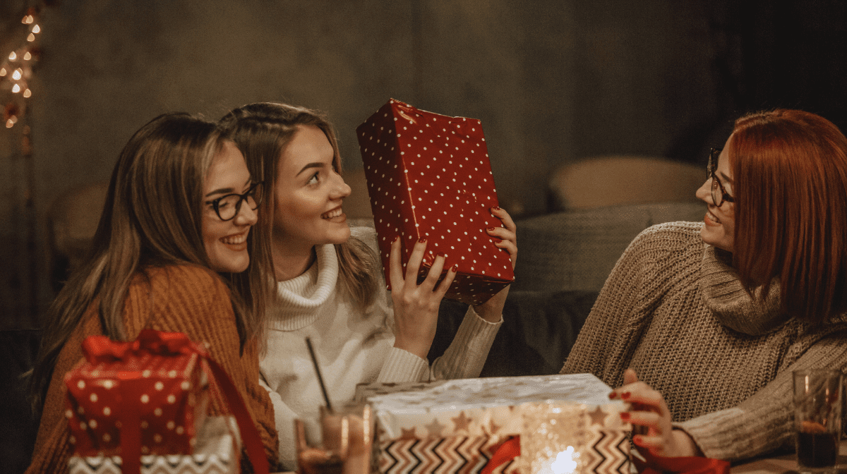 Three women exchange holiday gifts around a table | No7 Beauty US