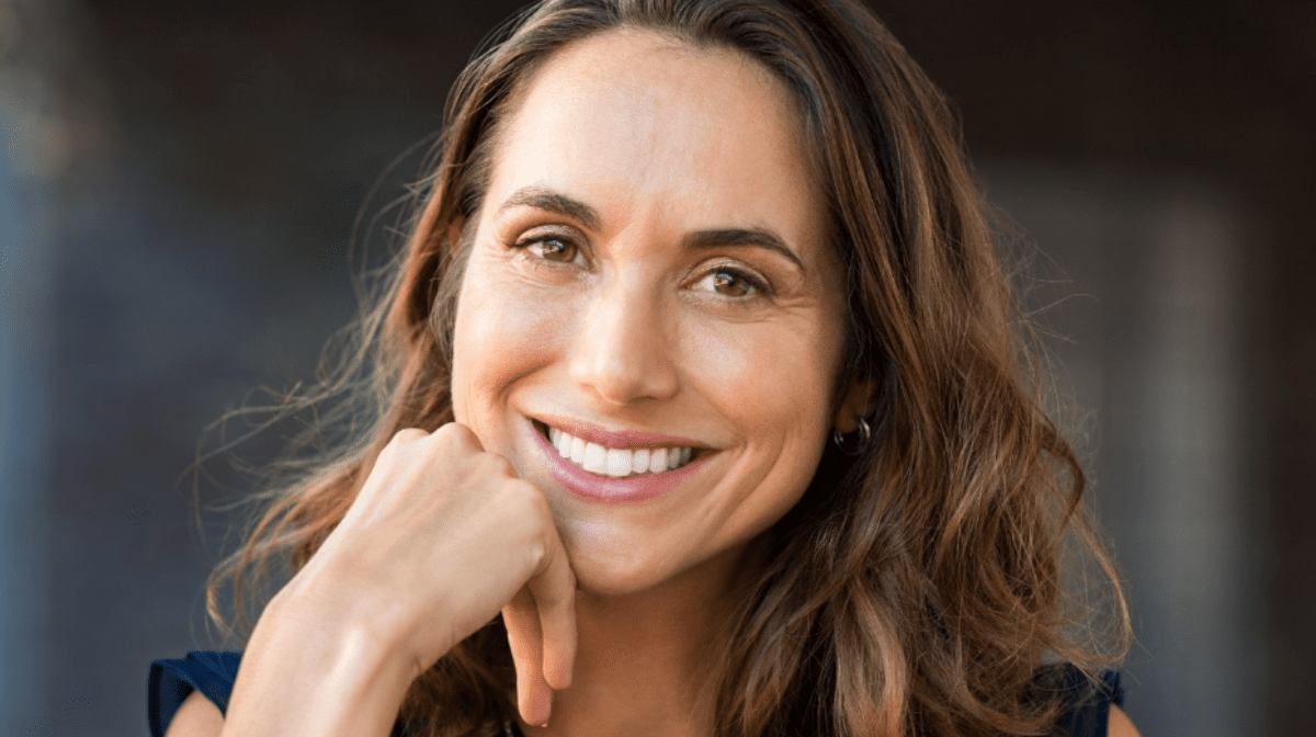 A brunette woman, with mouth wrinkles, smiles whilst wondering how to get rid of smile lines.