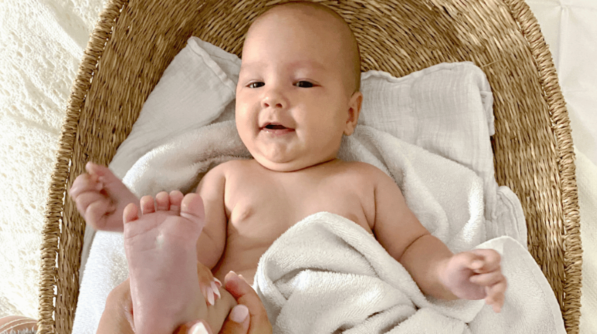 A baby lying down on a blanket having their foot massaged with Burt's Bees Nourishing Baby Oil