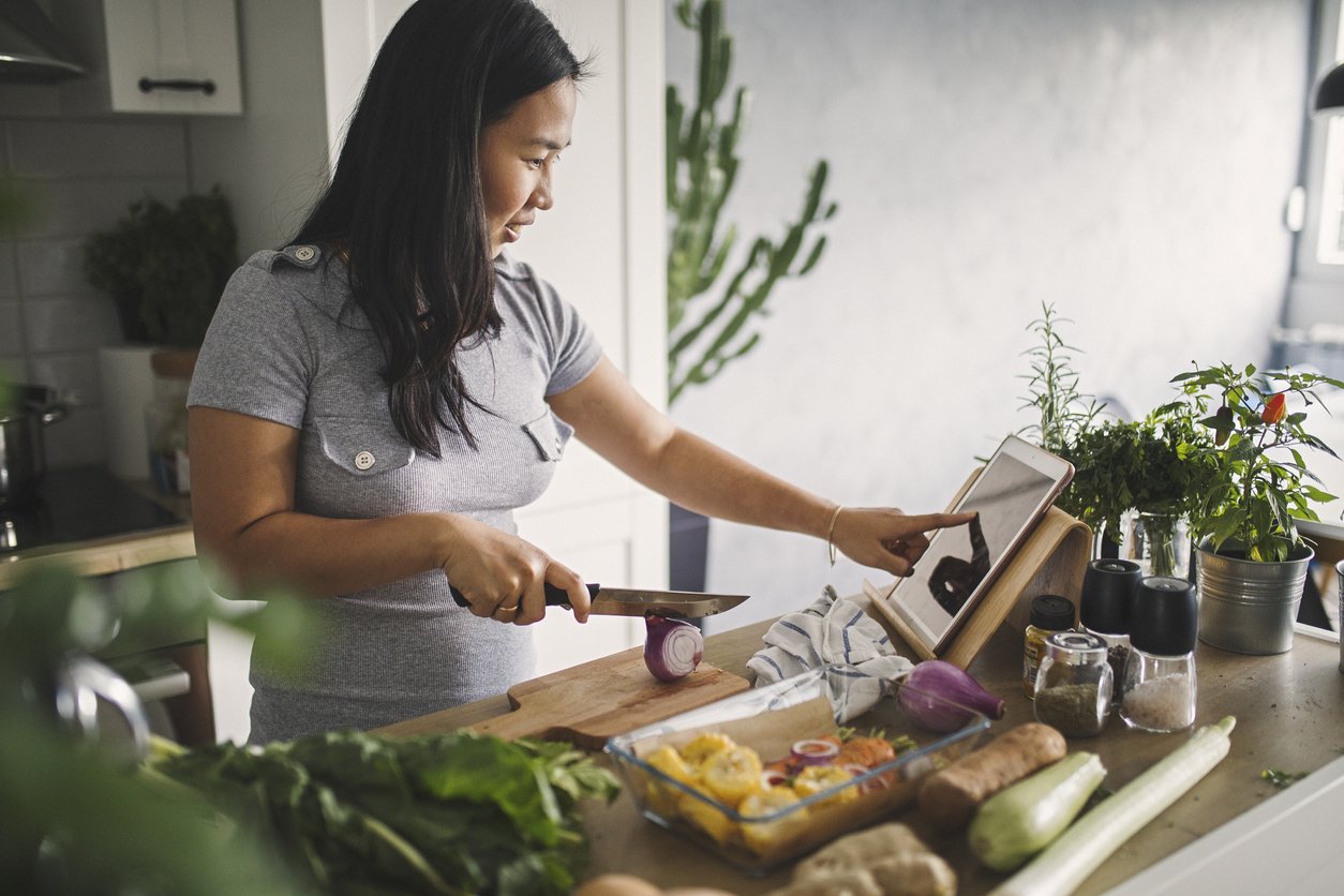 Image showing an overweight woman chopping vegetables and following a recipe, preparing a healthy meal as part of a balanced diet