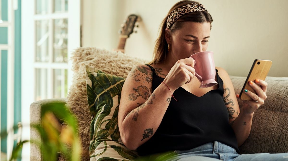 woman drinking from a mug while checking her phone