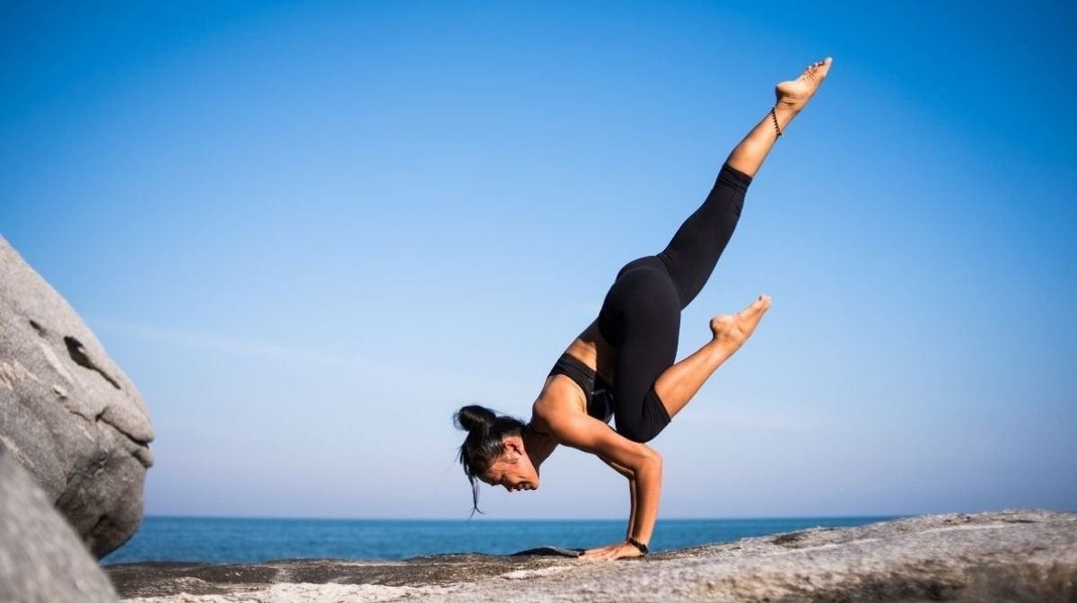 Una donna fa yoga su una collina rocciosa con il mare sullo sfondo.