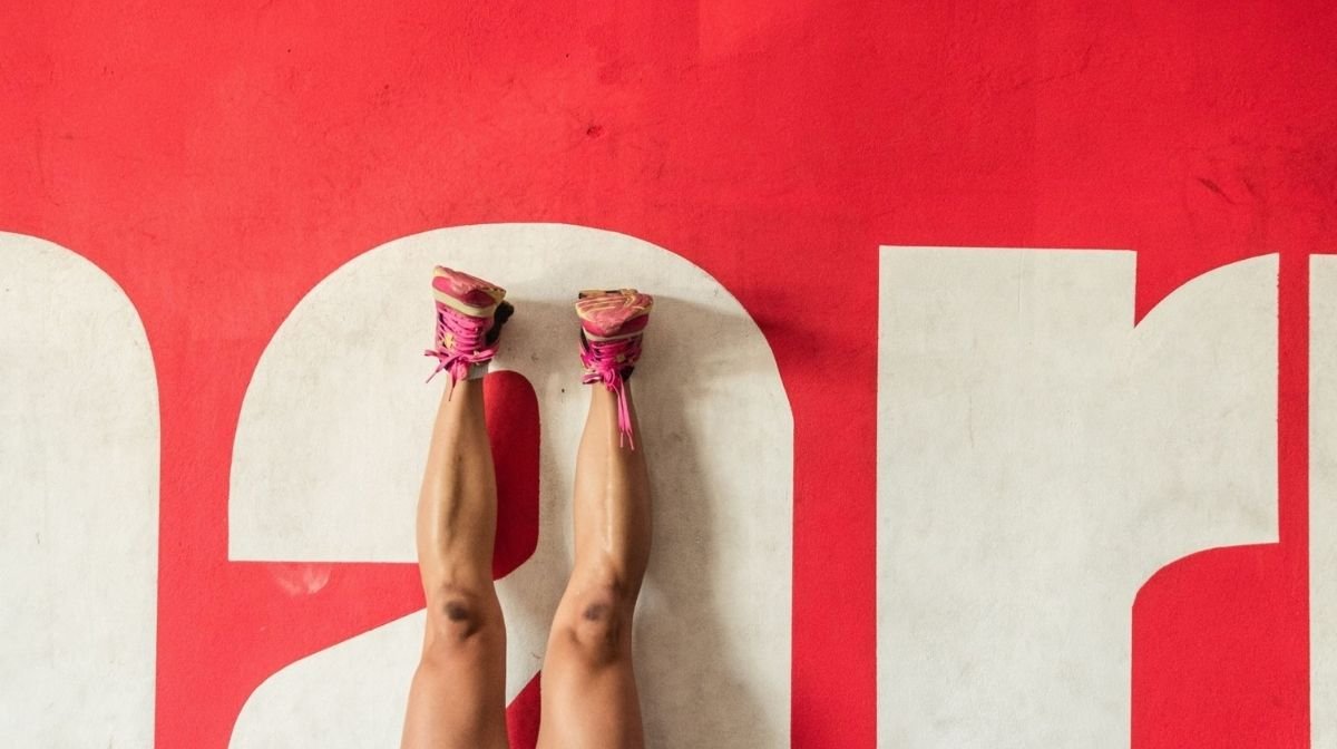 Piedi di una donna in scarpe da ginnastica rosa su un pavimento bianco e rosso.