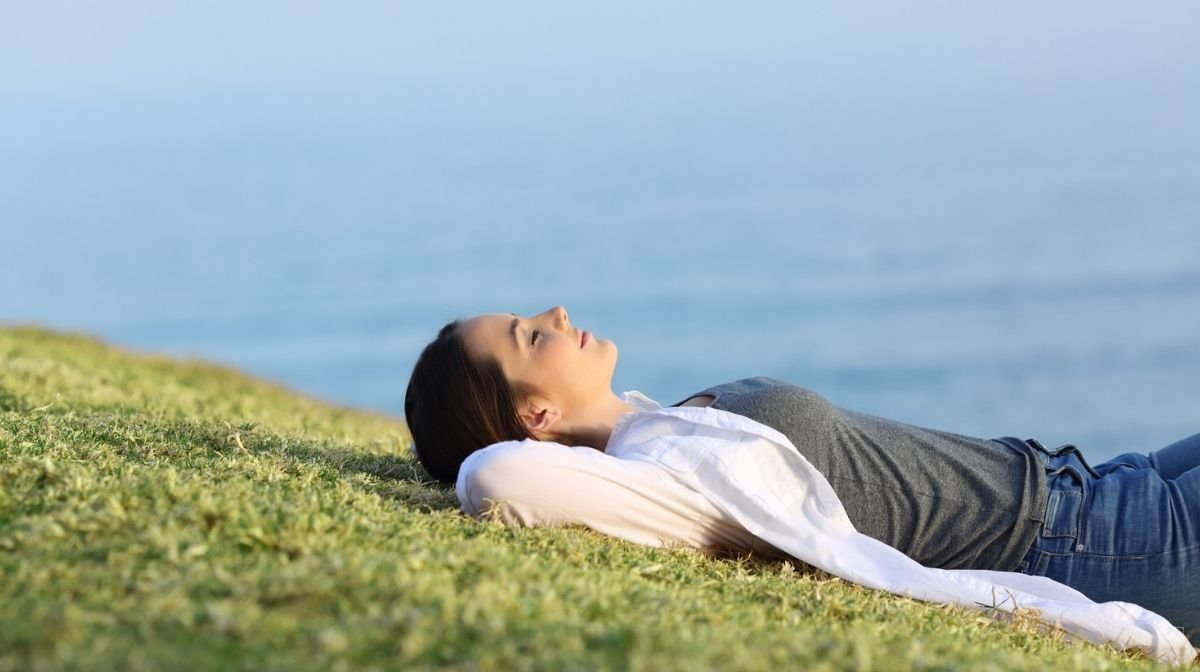 Una giovane donna che si rilassa sull'erba con il mare sullo sfondo.