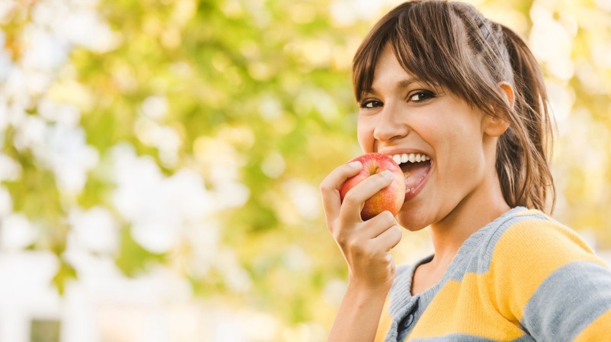 Una donna sorridente sta mangiando una mela in un giorno estivo.