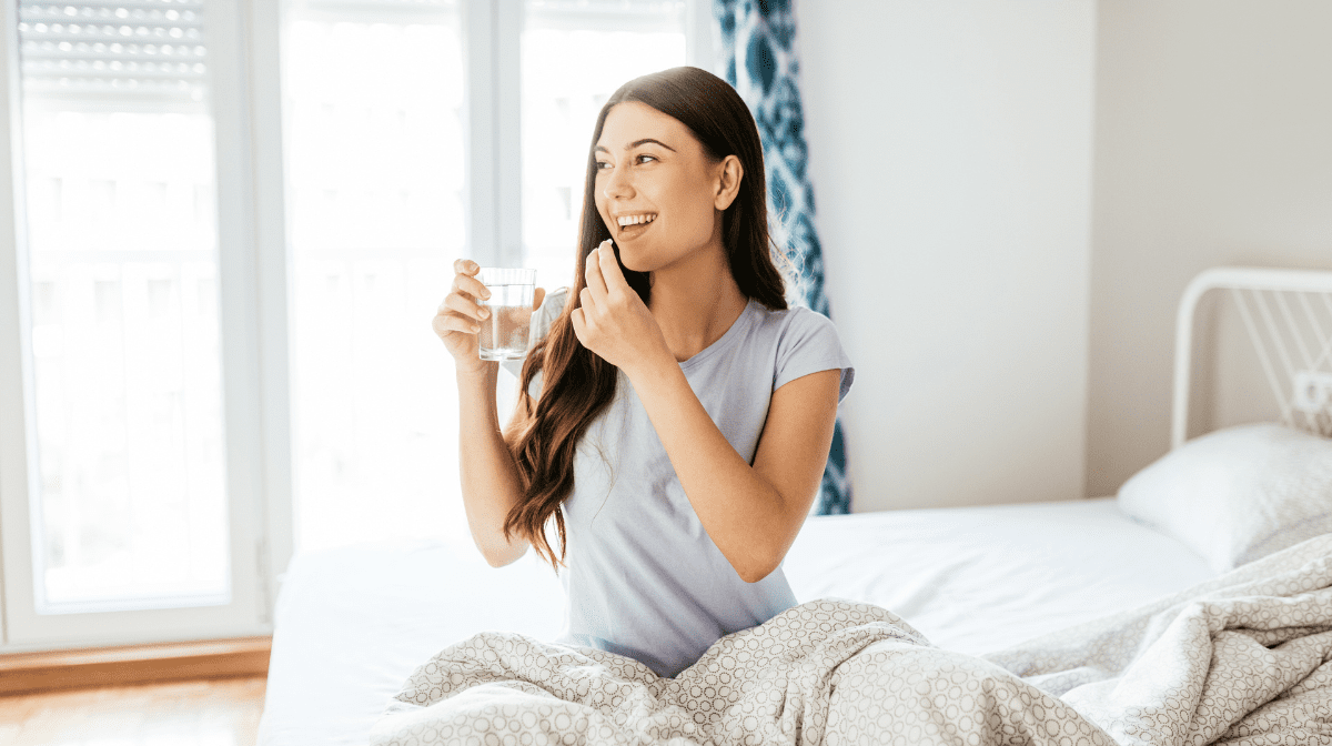 Women sat on bed with a glass of water taking period supplements
