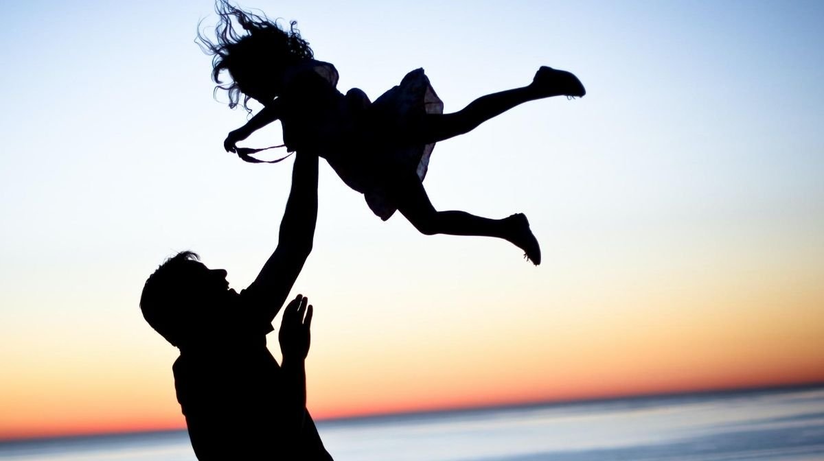 man throwing daughter in the air at the beach