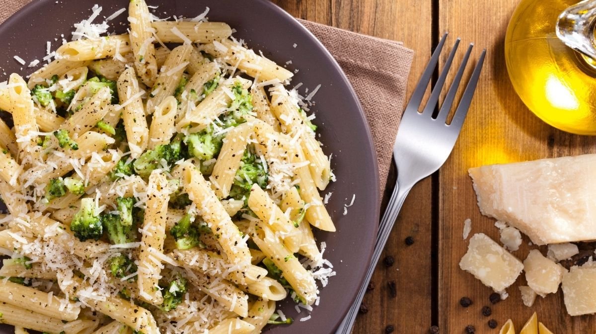 Birdseye view of penne pasta on a plate with anchovy sauce, broccoli and grated parmesan